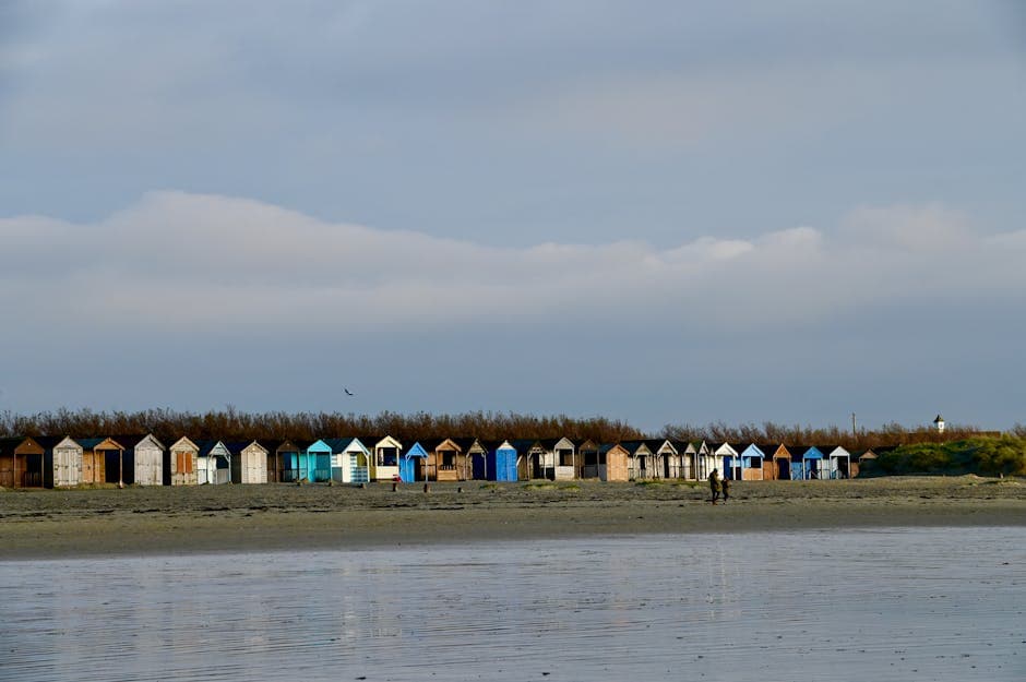 A picturesque row of colourful beach huts on a tranquil sandy beach under a cloudy sky
