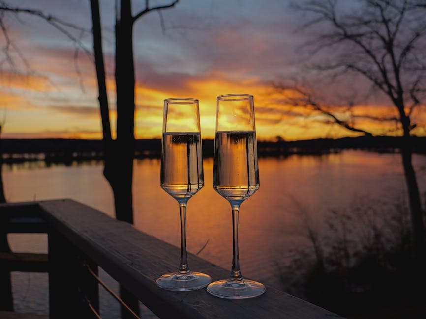 Two champagne glasses at sunset on a balcony overlooking calm water, celebrating a special occasion