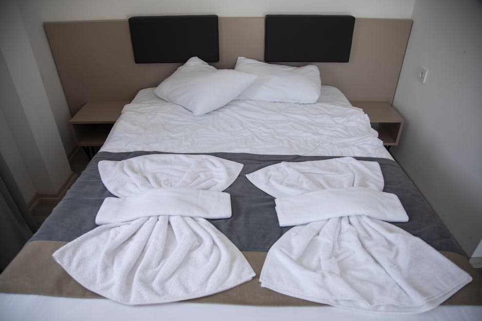 Neatly arranged hotel bedroom with a decorative towel display and bedside lamp