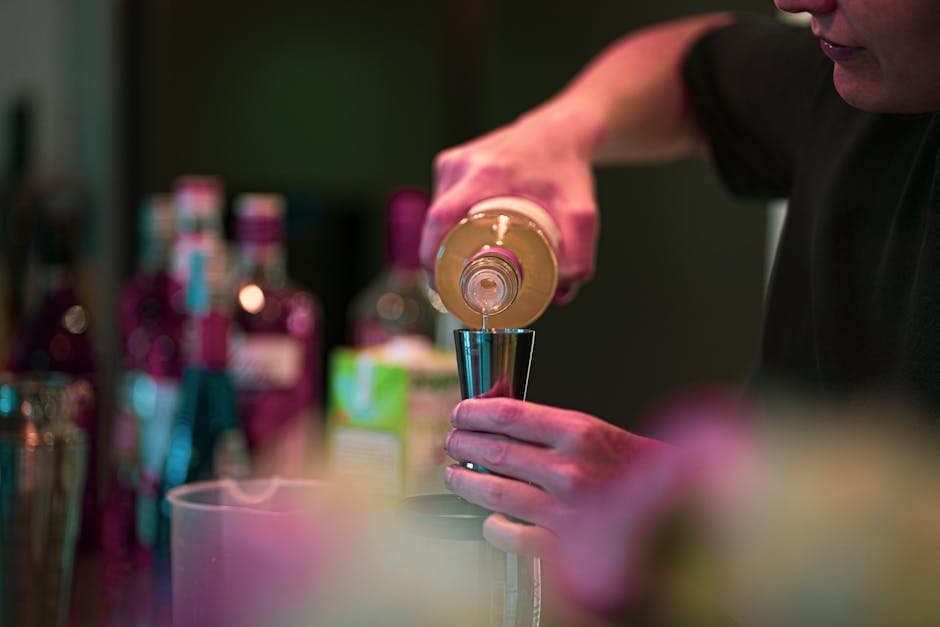 Bartender pouring a drink into a jigger at a stylish bar, preparing cocktails for a group evening