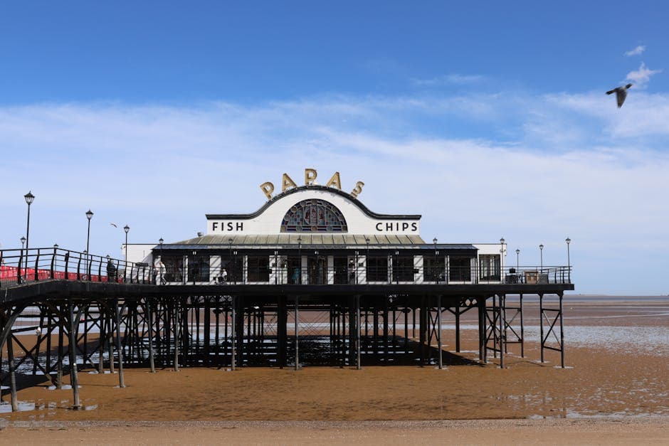 A classic British seaside pier with a fish and chips shop prominently visible under a clear blue sky