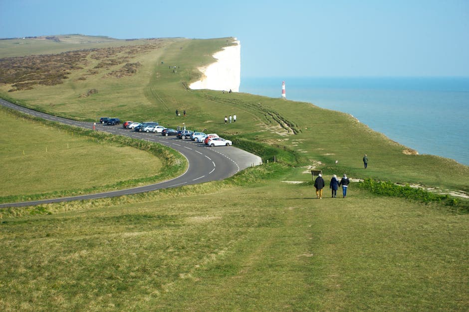 White chalk cliffs with green grass on top, overlooking a calm blue sea and sandy beach below