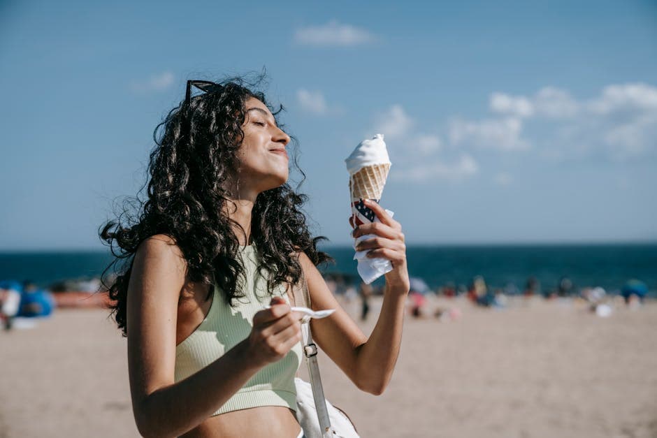 A woman enjoying an ice cream cone on the beach on a bright summer day