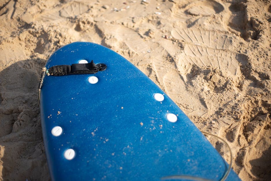 Blue foam surfboard resting on the sand at the beach, ready for a lesson or hire session