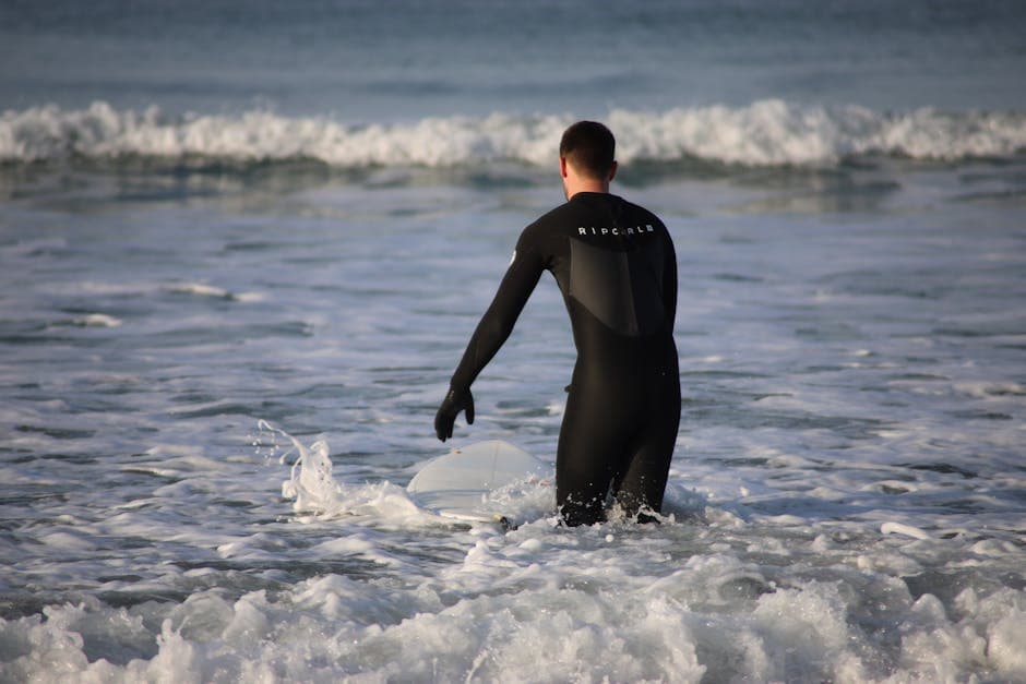 Surfer in a wetsuit standing on the beach with board, ready to paddle out into the waves