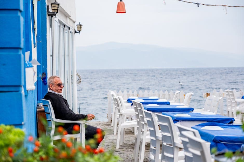 A man relaxing at a seaside cafe terrace with blue furniture and a view out over the water