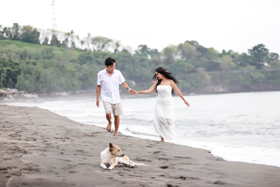 Couple joyfully walking on the beach with a dog on a bright sunny day by the coast