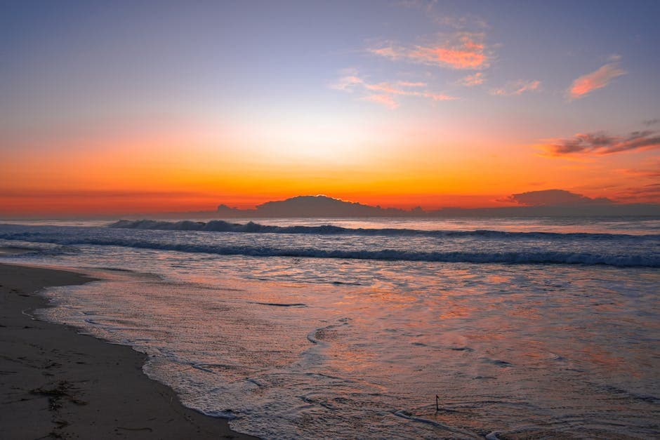 A vivid sunrise over a calm ocean with warm orange and pink light reflecting across the water