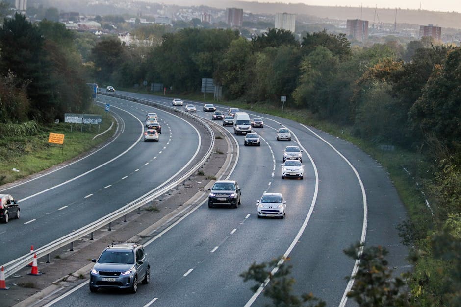 Cars travelling on a motorway with green hills and city buildings in the background