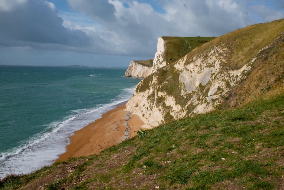 Dramatic chalk and limestone cliffs dropping to a turquoise sea along the Jurassic Coast, with a sandy beach below