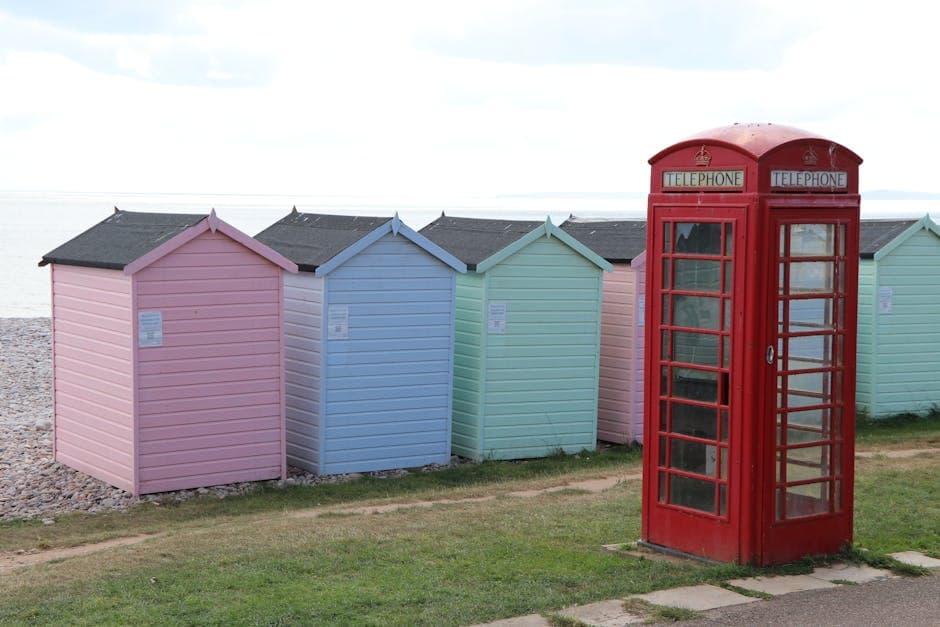 Colourful beach huts alongside a red phone box on an English seaside promenade, with sand and sea beyond