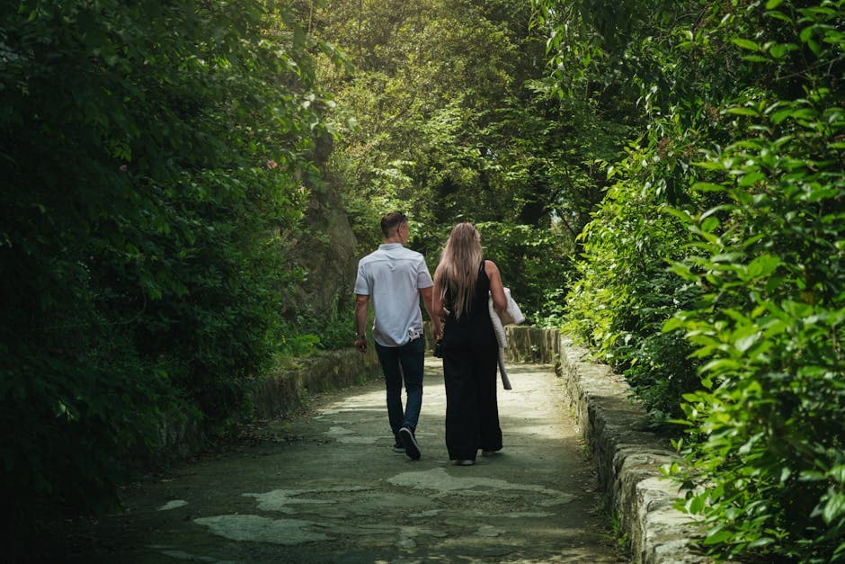 A couple walking hand in hand down a verdant forest path surrounded by lush greenery