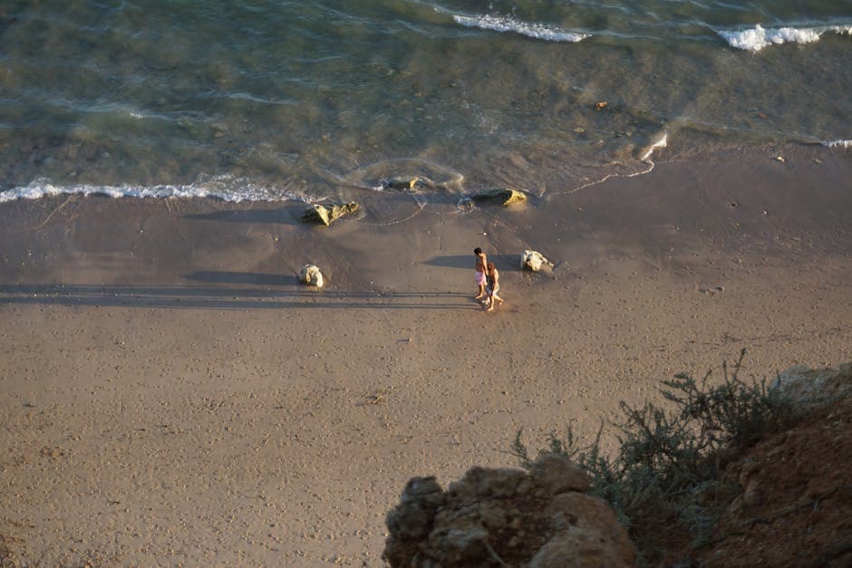 Aerial view of a couple walking along a sandy beach at sunset, the kind of evening walk that defines a coastal working stay