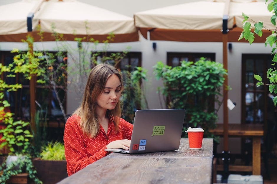 Young woman working on a laptop at an outdoor cafe with a coffee, enjoying a relaxed work-from-cafe session